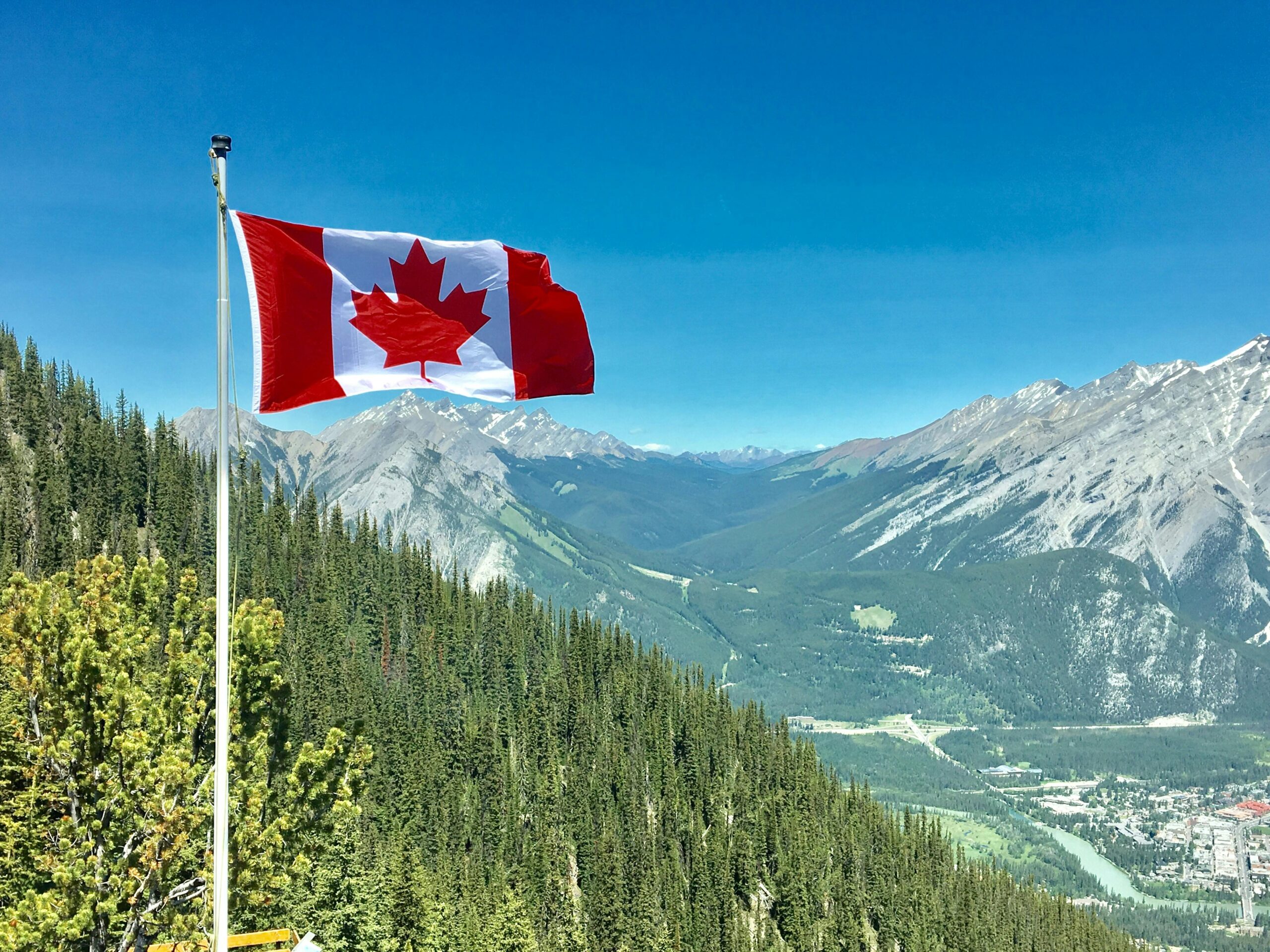 Canadian Flag waving in the wind against a beautiful Canadian mountain background on a clear, bluebird day